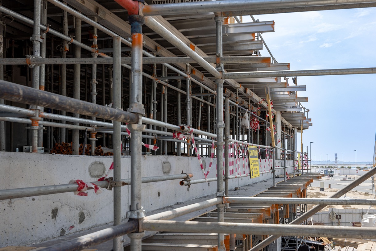Beach Walk Iii By Imtiaz A view of a construction site featuring scaffolding, concrete walls, and caution signage, under a clear sky.
